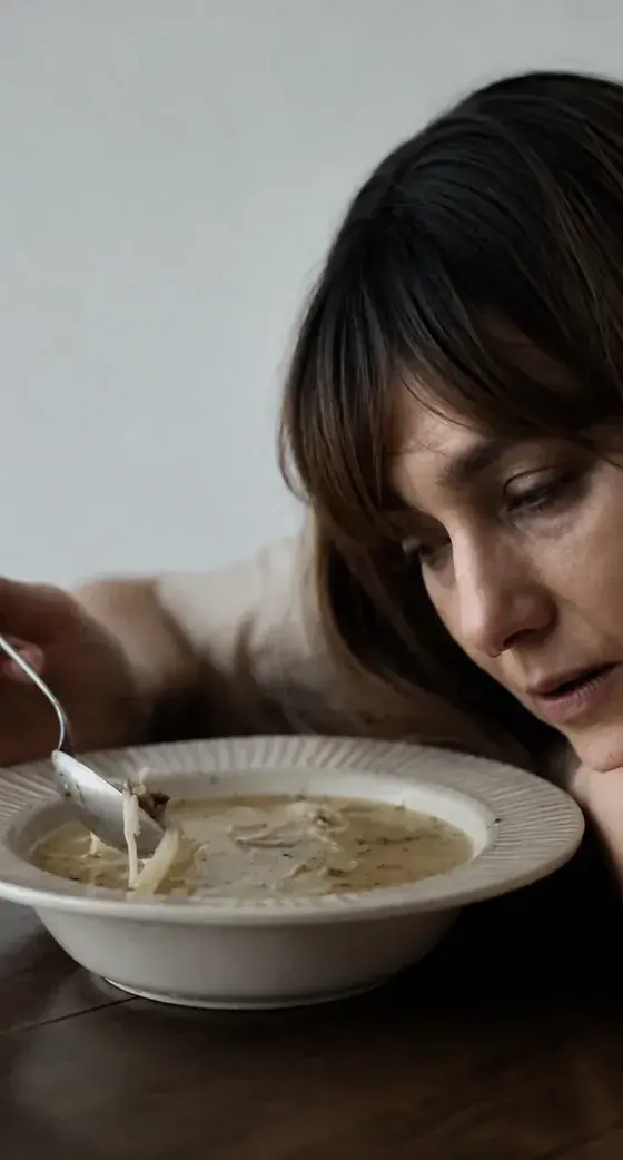 Mulher cabisbaixa diante de um prato de sopa, sem vontade de comer